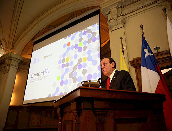 El rector Ignacio Sánchez hablando desde un podio, junto a la presentación de ConectIA.
