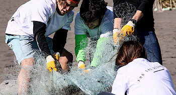 Un grupo de estudiantes retira redes de plástico de la playa.