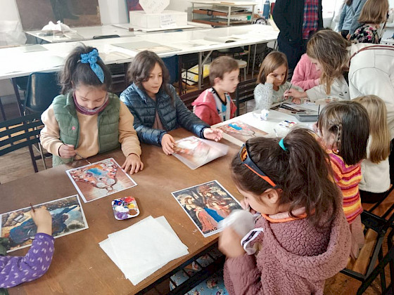 Niños sentados en una mesa sosteniendo dibujos.