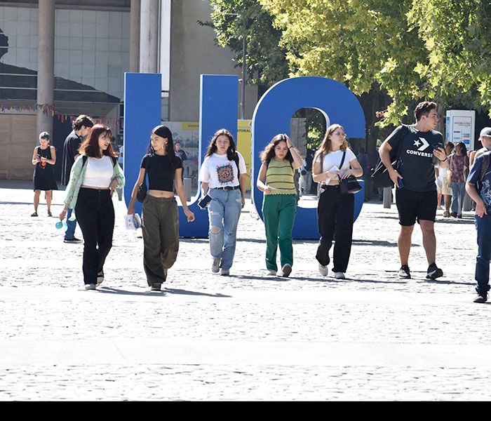 Jóvenes caminando en el campus San Joaquín con las letras UC en grande detrás
