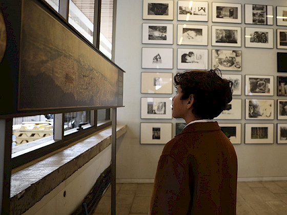 Niño observa una obra, al fondo se observa un muro con cuadros.