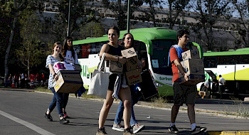Grupo de jóvenes sorientes llevando cajas hacia los buses.