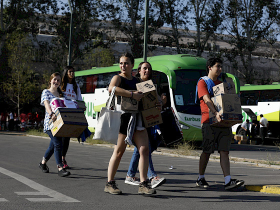 Grupo de jóvenes sorientes llevando cajas hacia los buses.