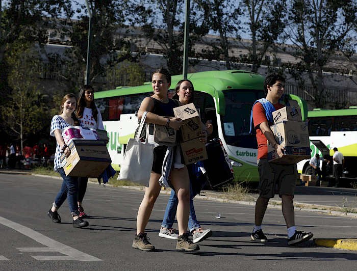 Grupo de jóvenes sorientes llevando cajas hacia los buses.