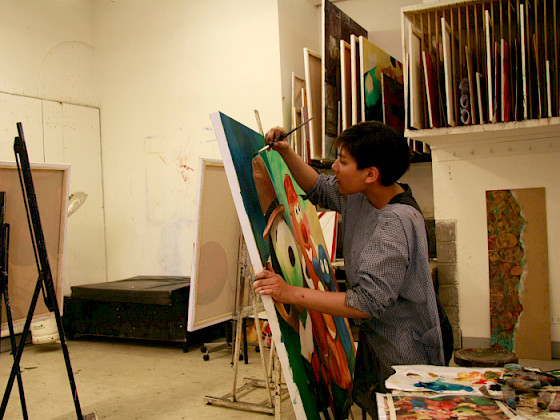 Mujer pintando una tela sobre atril.