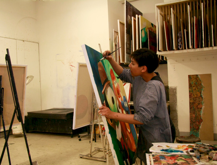 Mujer pintando una tela sobre atril.