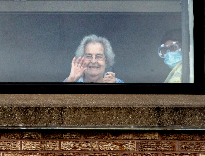 Mujer de la 3a edad saluda desde la ventana.