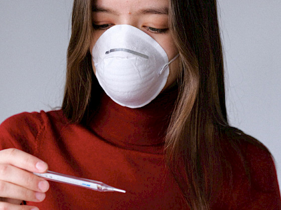 Mujer con mascarilla y sosteniendo un termómetro