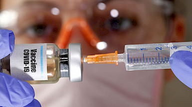Primer plano de una aguja entrando en un frasco que dice Vacuna Covid-19