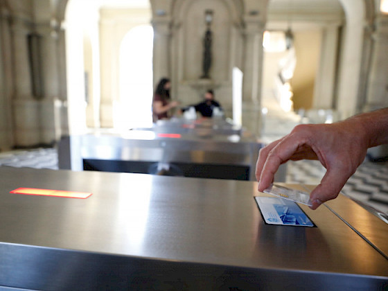 Una mano acercando tarjeta UC TUC al lector de un torniquete en el hall central de Casa Central.