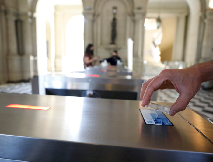 Una mano acercando tarjeta UC TUC al lector de un torniquete en el hall central de Casa Central.