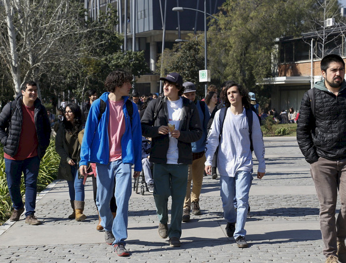 Jóvenes caminan en patio de campus universitario. 