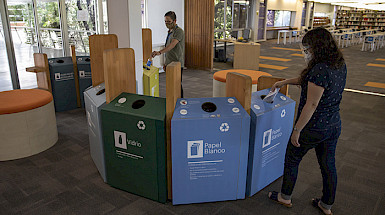 Foto que muestra receptáculos coloridos de reciclaje de papel y otros materiales en la biblioteca San Joaquín del campus homónimo.