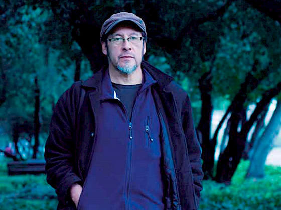 Fotografía de hombre con barba, boina, anteojos. Lleva chaqueta azul