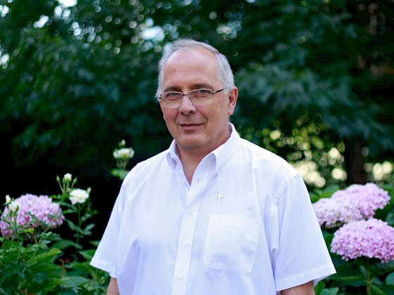 Se ve un hombre de pelo blanco, anteojos y camisa blanca.