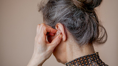 Se visualiza mujer adulto mayor poniéndose un audífono en la oreja.