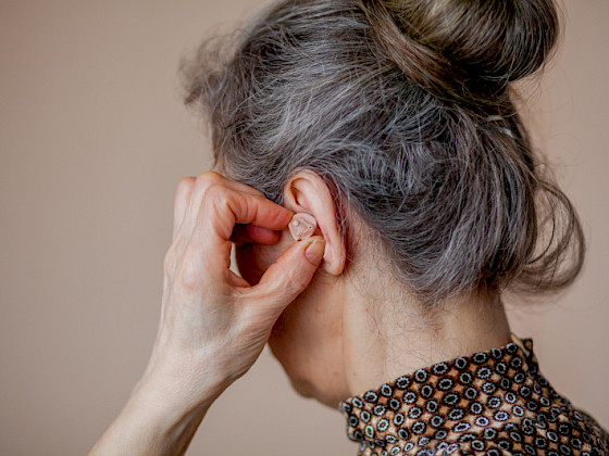 Se visualiza mujer adulto mayor poniéndose un audífono en la oreja.