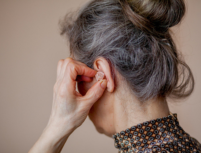 Se visualiza mujer adulto mayor poniéndose un audífono en la oreja. 