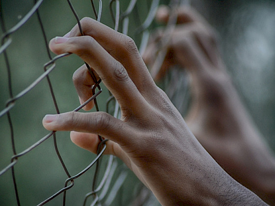 Foto de unas manos agarradas de una reja