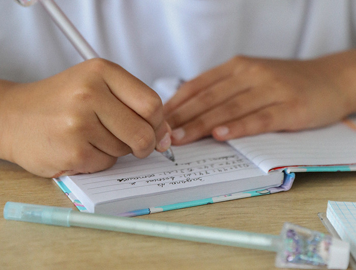 Manos de niño escolar escribiendo sobre un cuaderno.