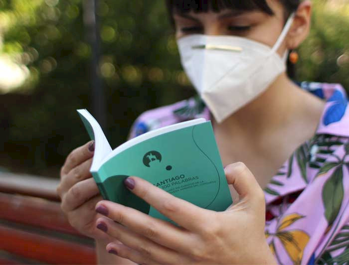 Imagen de veinteañera leyendo en un parque, con mascarilla, uno de los libros recopilatorios con cuentos breves del concurso Santiago en 100 palabras.