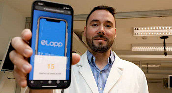 Médico y académico de la UC, con cotona blanca, muestra en su celular la aplicación que creo para hacer simulación médicas a distancia.