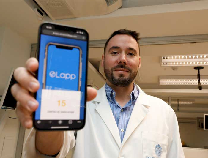 Médico y académico de la UC, con cotona blanca, muestra en su celular la aplicación que creo para hacer simulación médicas a distancia. 