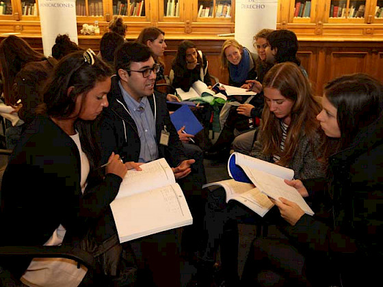 Image of a student orientation before the pandemic. Credits: César Cortés. Alt: Group of international students and a UC counselor in the Manuel José Yrarrázaval hall, Casa Central.