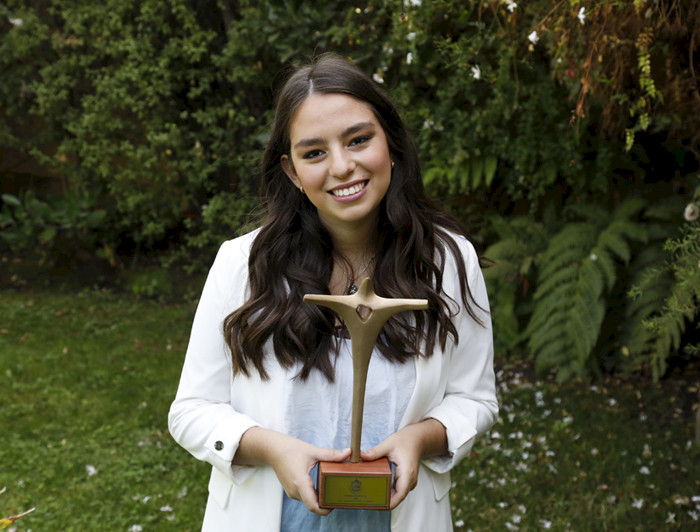 La estudiante María de los Ángeles Ossorio, Premio Espíritu UC 2021, en el patio de su casa, sostiene un Cristo metálico como galardón.