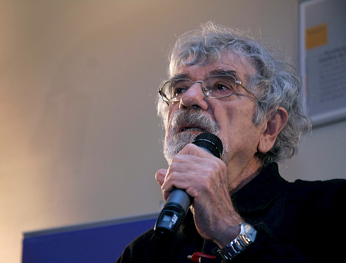 hombre con pelo canoso, barba blanca y anteojos, hablando con un microfono en la mano