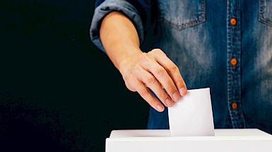 A hand inserts a vote into a ballot box.