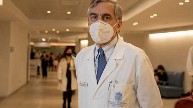 El decano de Medicina, Felipe Heusser, con bata blanca y mascarilla en un pasillo del hospital de calle Marcoleta.