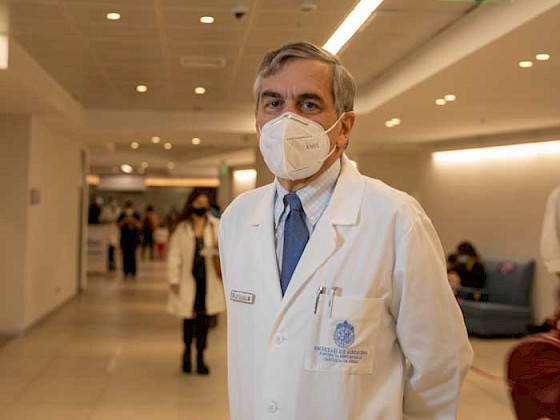 El decano de Medicina, Felipe Heusser, con bata blanca y mascarilla en un pasillo del hospital de calle Marcoleta.