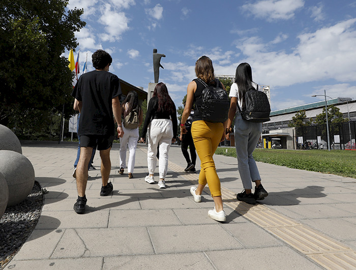 Imagen de las espaldas de un grupo de estudiantes en campus San Joaquín que sale del Centro de Innovación en un día soleado. 