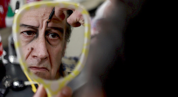 Actor Willy Semler se mira en un espejo de mano, mientras revisa su maquillaje durante la producción de la obra de Teatro UC, Muerte Accidental de un Anarquista.