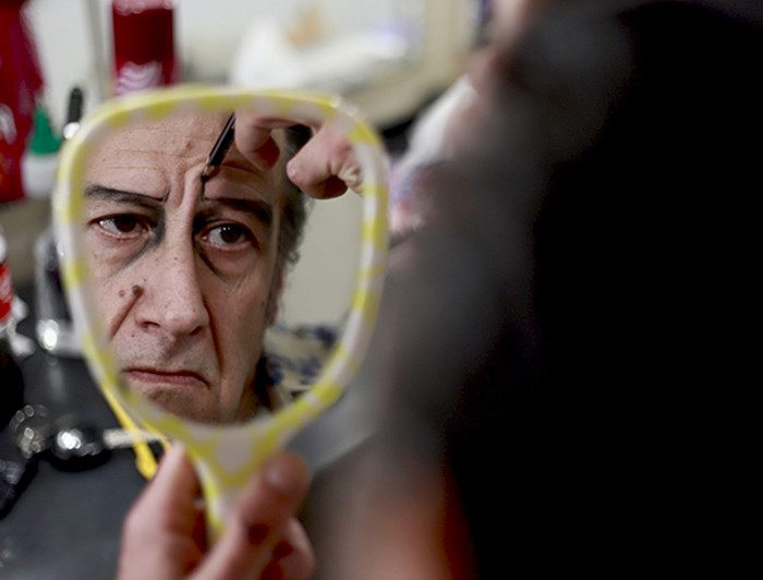 Actor Willy Semler se mira en un espejo de mano, mientras revisa su maquillaje durante la producción de la obra de Teatro UC, Muerte Accidental de un Anarquista.