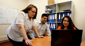 Tres funcionarios de la Vicerrectoría de Comunicaciones (dos mujeres y un hombre) revisan una información en un computador.