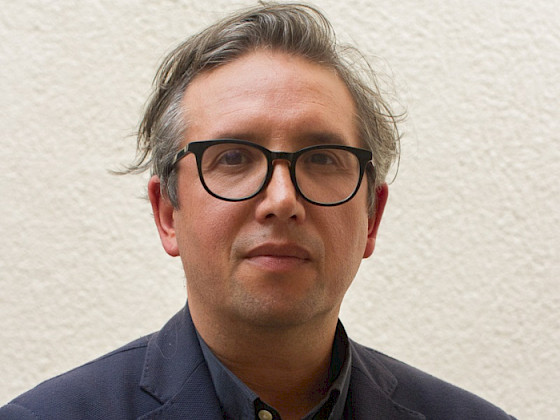 Foto retrato a Manuel Tironi, hombre, de frente, lentes negros, chaqueta azul.