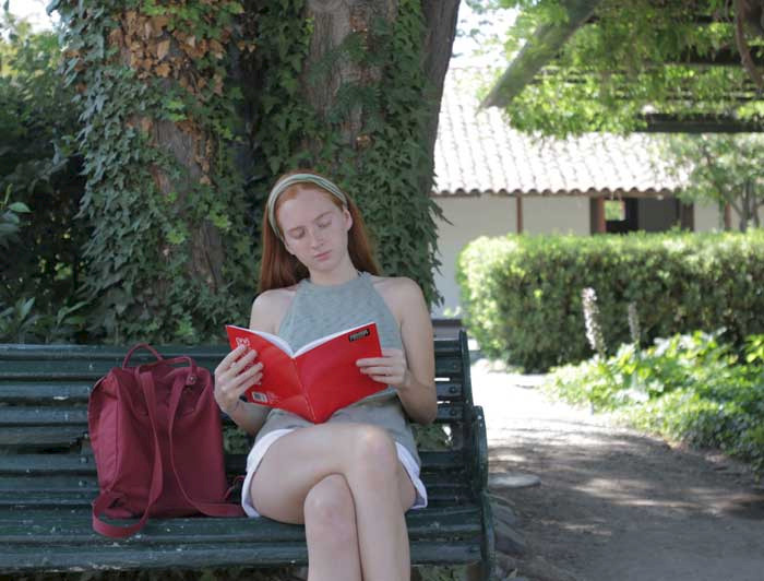 Estudiante mujer leyendo sus apuntes en un banco del campus Lo Contador.