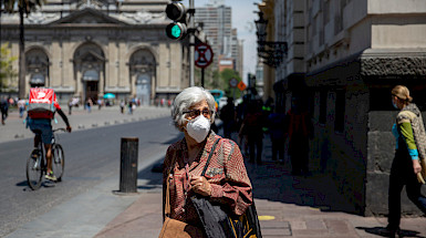 Mujer, persona mayor, pelo canoso, de frente, caminando en el centro de Santiago, usando mascarilla blanca.