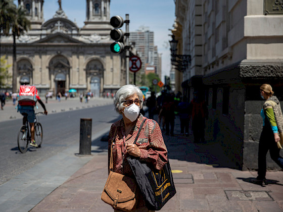 Mujer, persona mayor, pelo canoso, de frente, caminando en el centro de Santiago, usando mascarilla blanca.