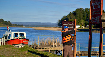 hombre frente a un lago y a una lancha señalando un letrero