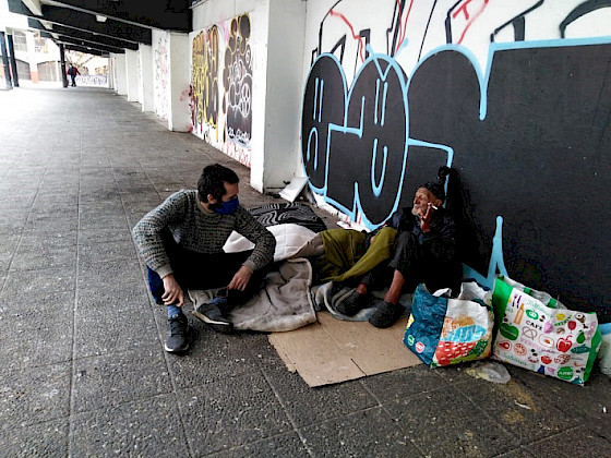 Estudiante de la UC junto a un hombre en situación de calle de la plaza El Pedregal de calle Portugal.