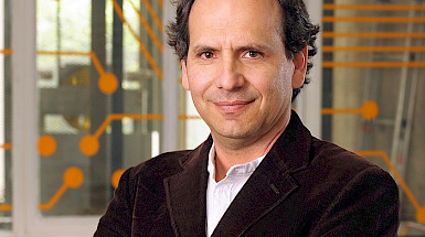 Patricio de la Cuadra in a brown jacket standing in front of an orange wall