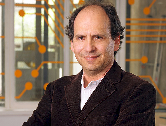 Patricio de la Cuadra in a brown jacket standing in front of an orange wall