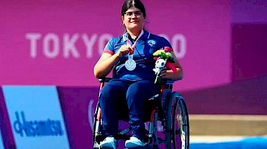 Deportista y estudiante en silla de ruedas mostrando su medalla de plata ante las cámaras.