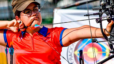 a woman in a red shirt is holding a bow and arrow