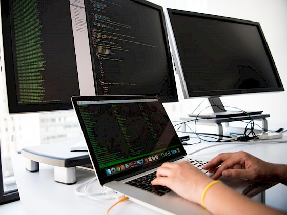 manos de joven en un computador frente a 4 pantallas