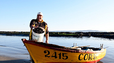 Pescador junto a su bote mostrando un balde con moluscos.