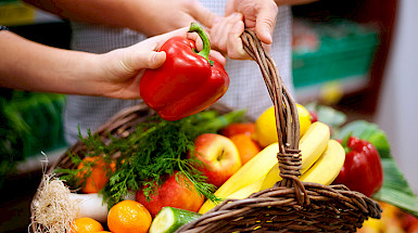 Mano sostiene un pimentón rojo sobre una canasta llena de frutas y verduras.